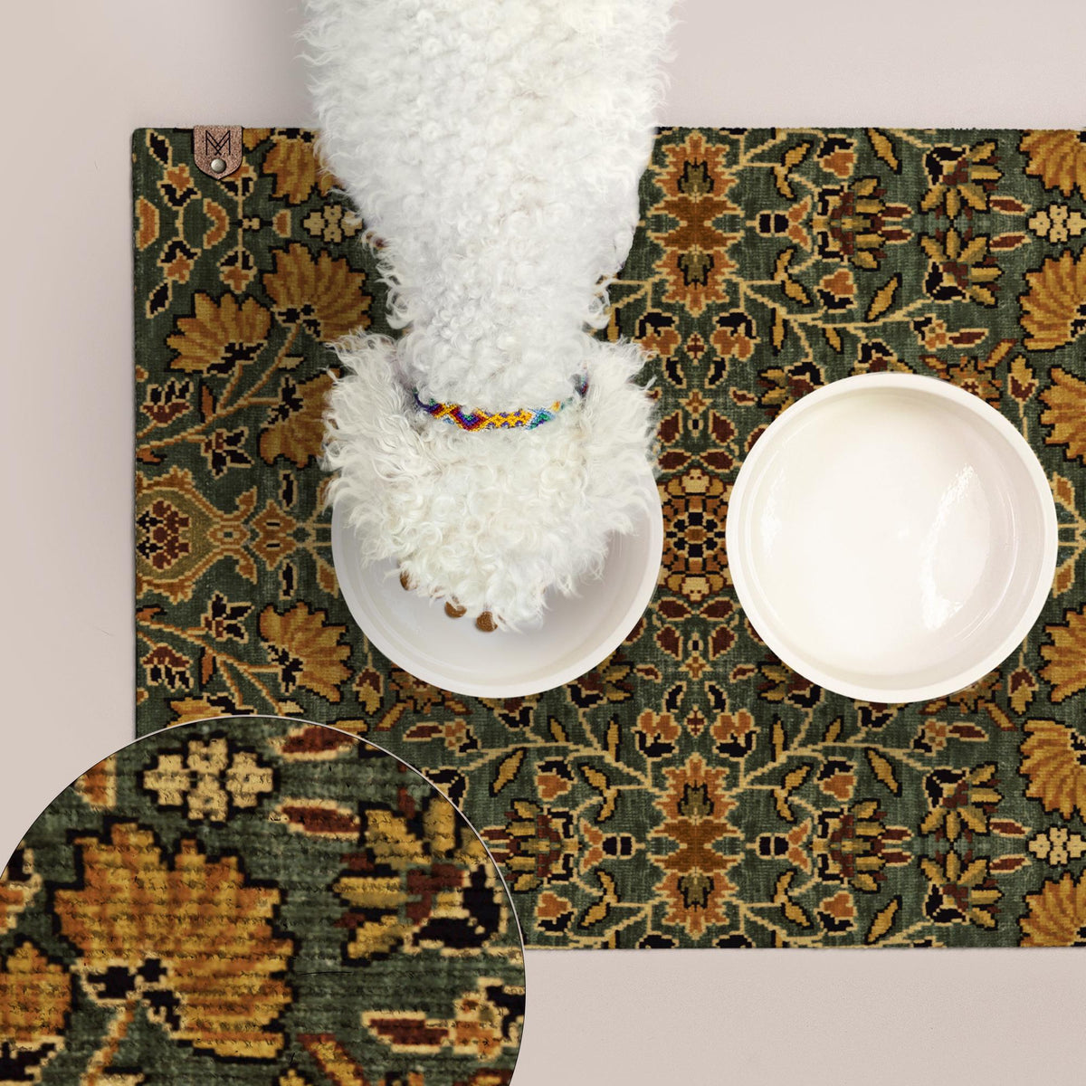 A white dog is standing on a green and gold patterned mat, with two empty bowls placed on the mat.