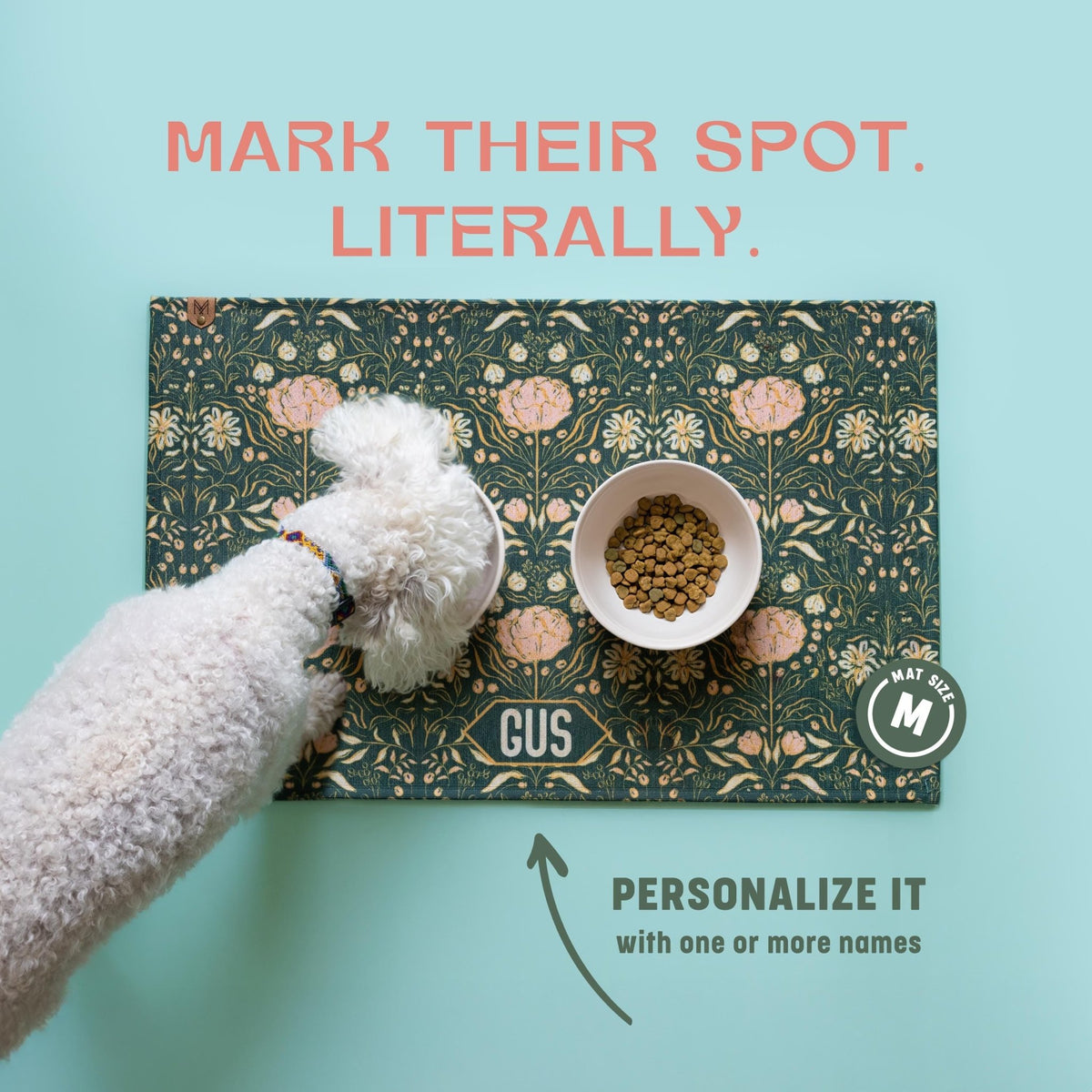 A white dog is standing next to a bowl of food on a patterned mat, with text above the mat that reads "Mark their spot. Literally."